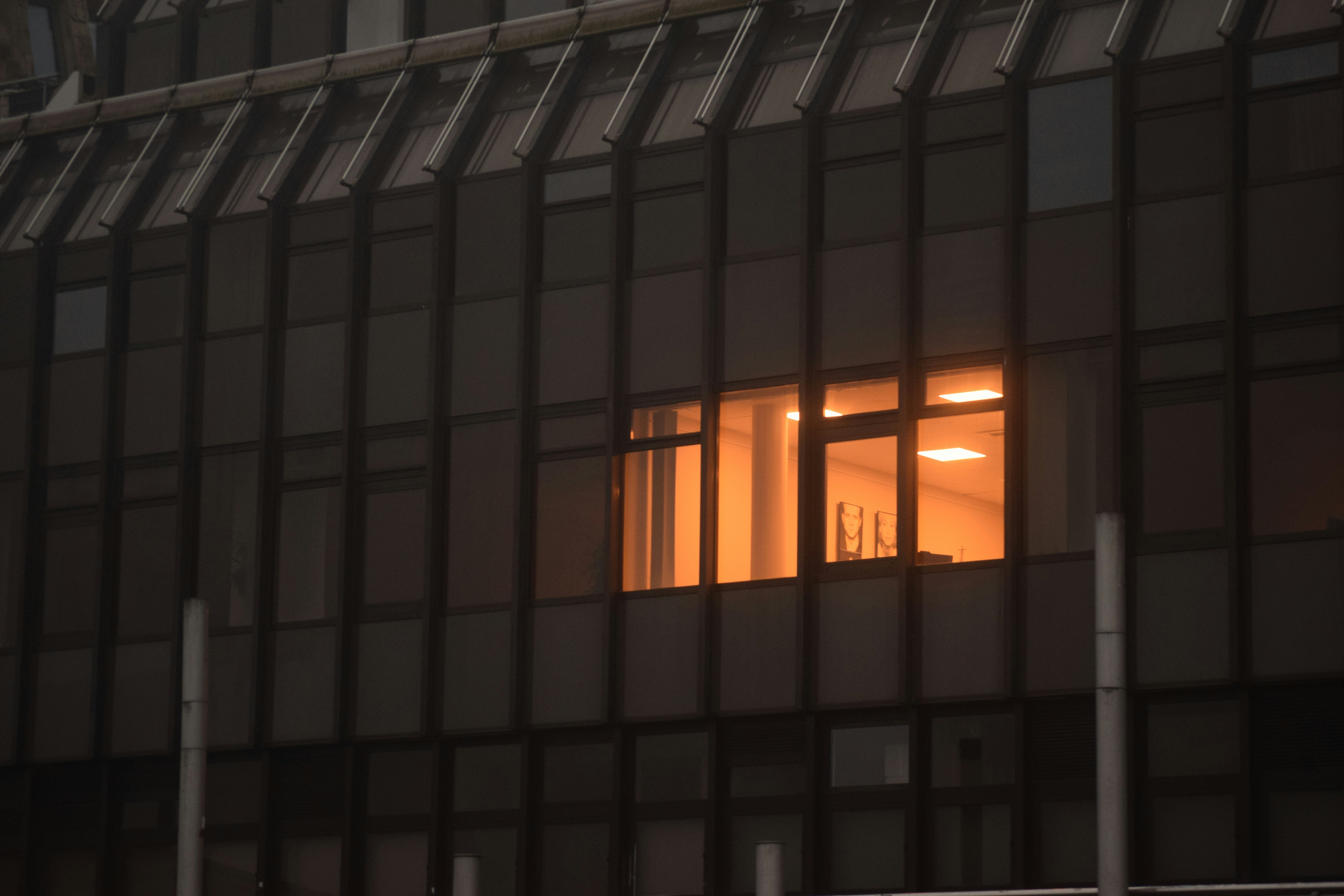 A single warm-lit window glowing in a dark facade of identical windows